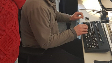 Einen Brief nur mit Hilfe eines Screenreaders verfassen ist gar nicht so einfach. Eine männliche Person sitz an einem Schreibtisch und drei weitere Personen stehen drum herum und schauen zu.
