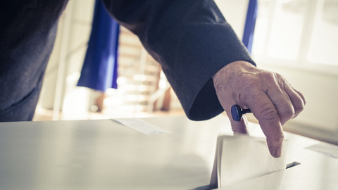 Eine Person wirft einen Wahlzettel in eine Wahlurne.