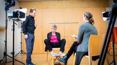 Eine Vorbereitung auf ein Interview. In der Mitte sitzt Frau Degener. Vor ihr sitzt Frau Roth, die Interviewerin. Links von Frau Degener steht ein Mann.