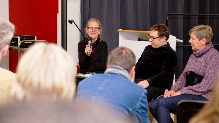 Martina Siehoff (auf dem Podium links) und Regine Bewer (auf dem Podium rechts) berichten von ihren Erfahrungen mit dem Persönlichen Budget. Das Gespräch wird moderiert von Manuel Salomon vom KSL Arnsberg (auf dem Podium in der Mitte).