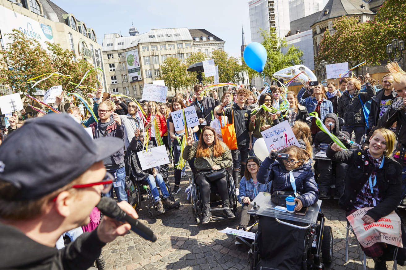 Das Foto zeigt Menschen bei der Kundgebung zum Protesttag am 5. Mai 2019 auf dem Münsterplatz Bonn. Foto: Aktion Mensch