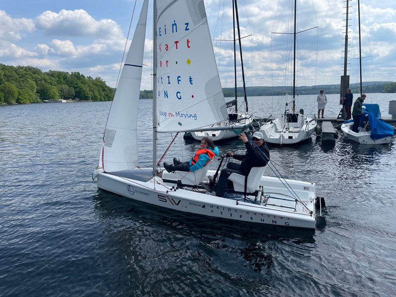 Zwei Personen in einem Segelboot, auf dem auch mit Menschen mit körperlichen Einschränkungen den Sport betreeiben können.